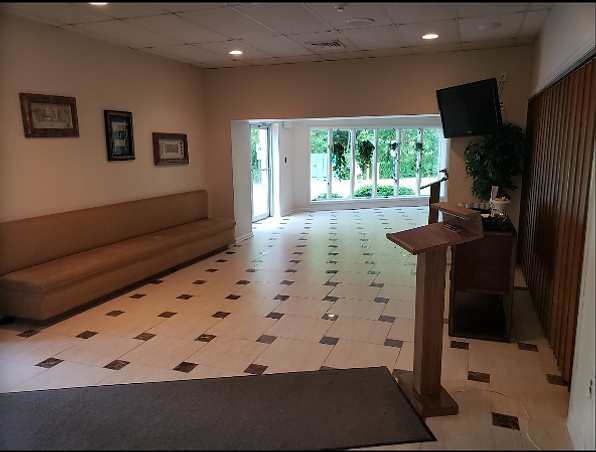 Empty lobby with tiled floor, long bench seating, and glass doors opening to greenery outside
