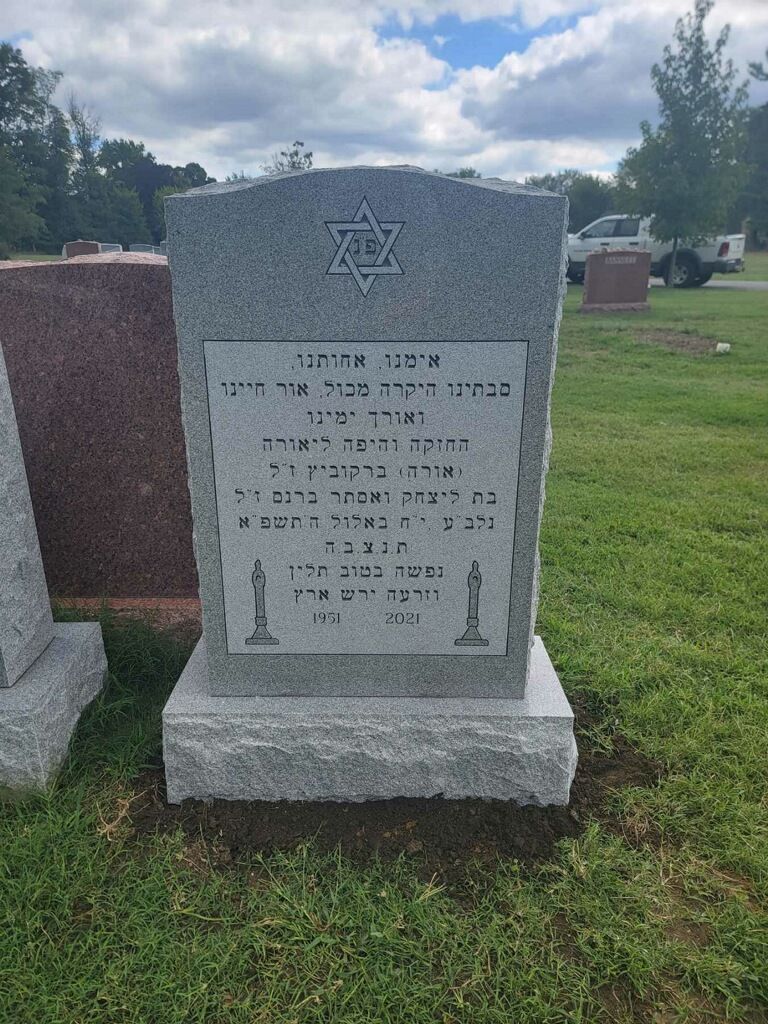 Gray Hebrew gravestone with Star of David in a cemetery under a cloudy sky.