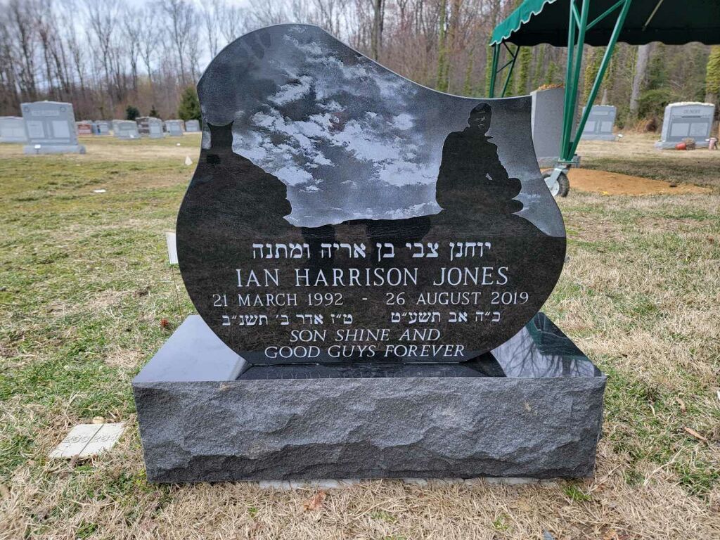 Black granite gravestone with Hebrew and English inscriptions in a grassy cemetery.