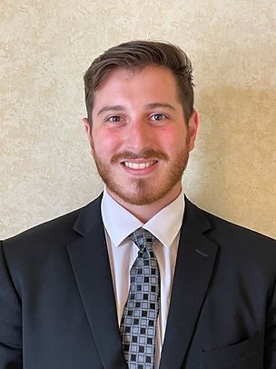 Smiling man in a black suit, white shirt, and patterned tie against a beige background