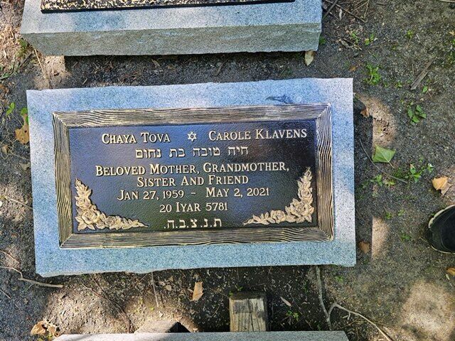 Blue grave marker with gold lettering lying on the ground amid grass and dirt