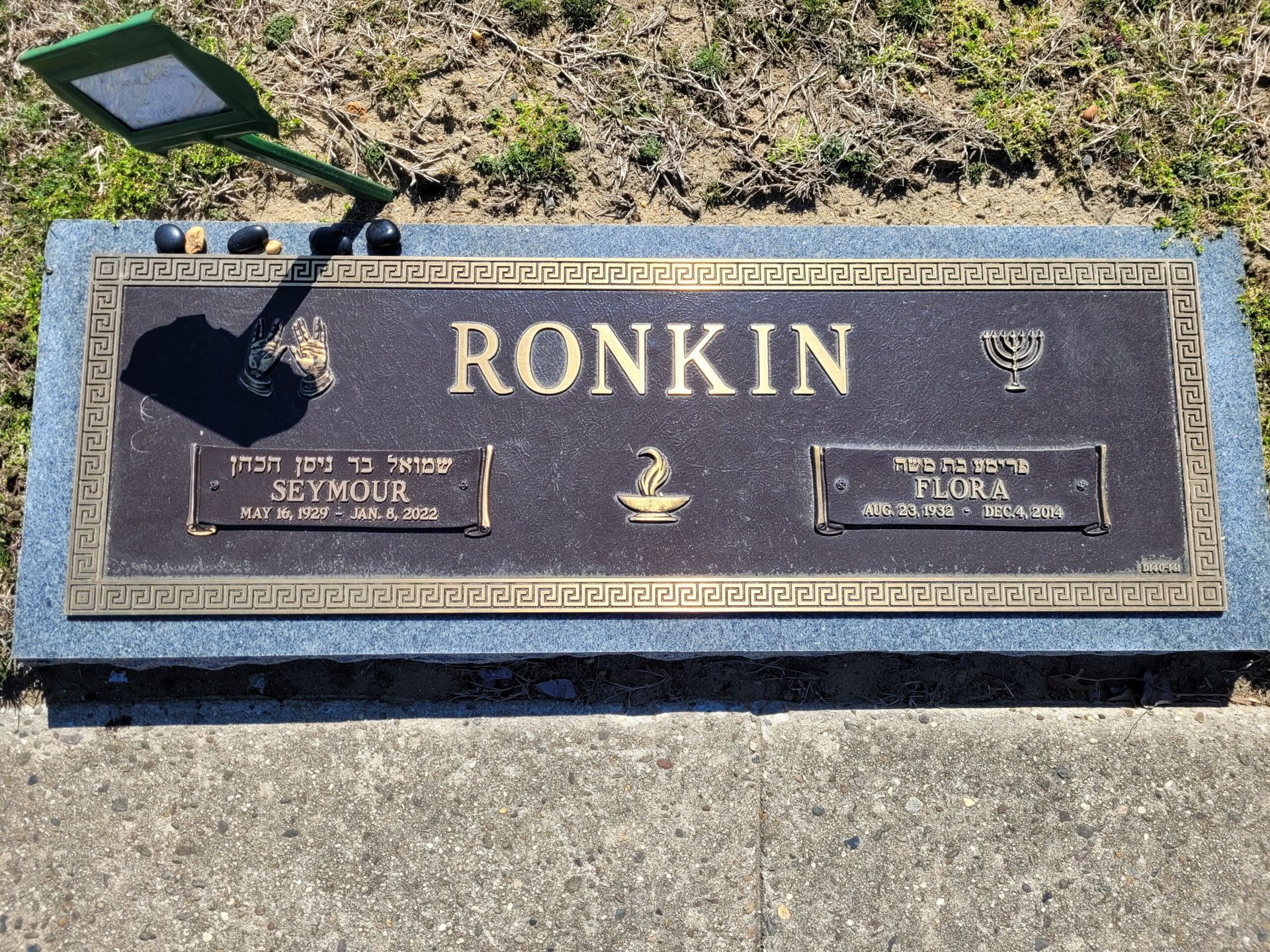 Bronze grave marker for Ronkin with engraved plaques and a solar light beside it in a cemetery.