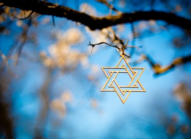 Gold Star of David ornament hanging from a branch against a blurred blue sky