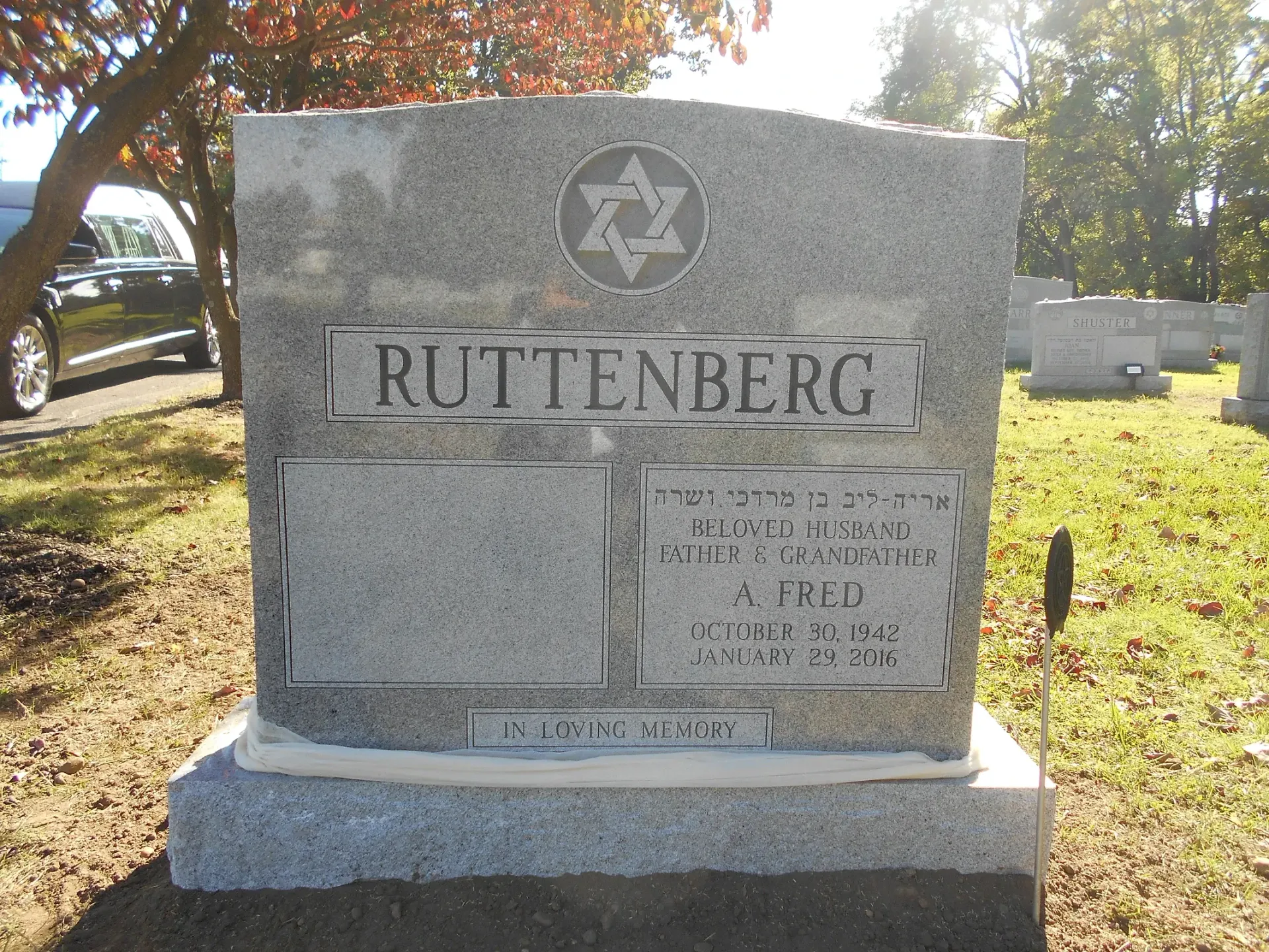 Granite gravestone with the name RUTTENBERG in a sunny cemetery, with trees and other headstones nearby.