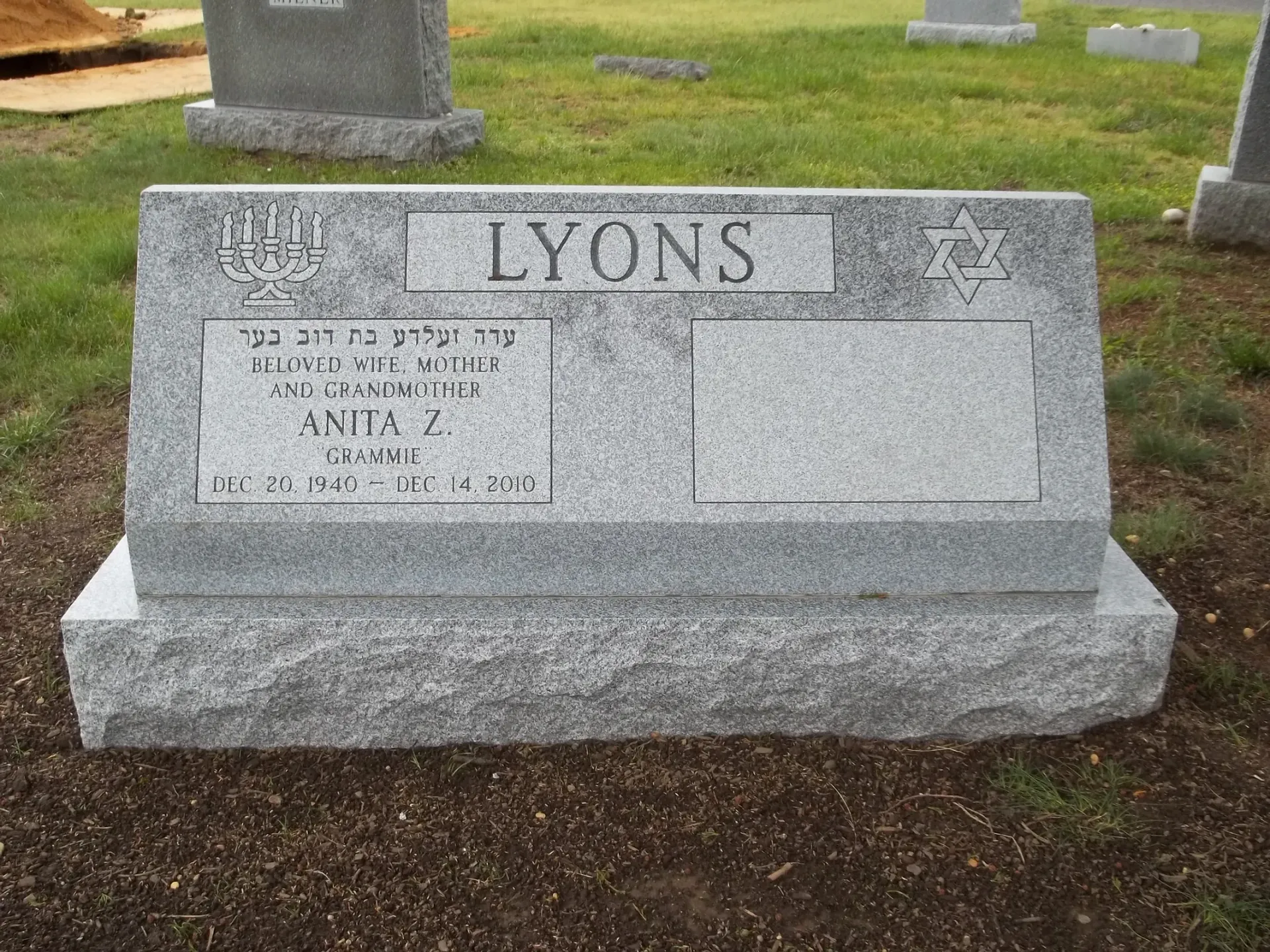 Gray granite gravestone engraved “LYONS” in a cemetery with grass and other headstones nearby