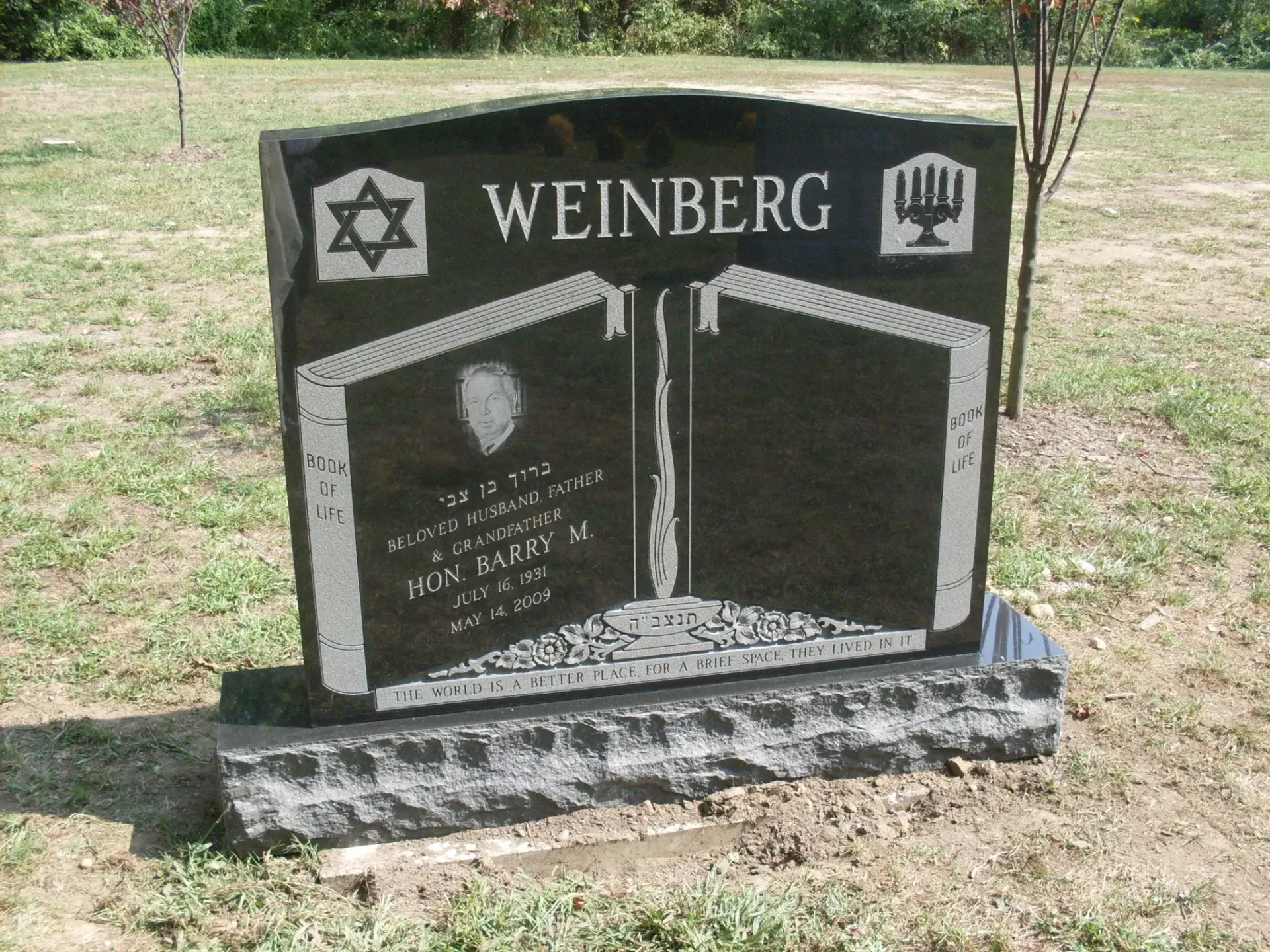 Black granite Jewish memorial headstone with Star of David, set in a grassy cemetery.
