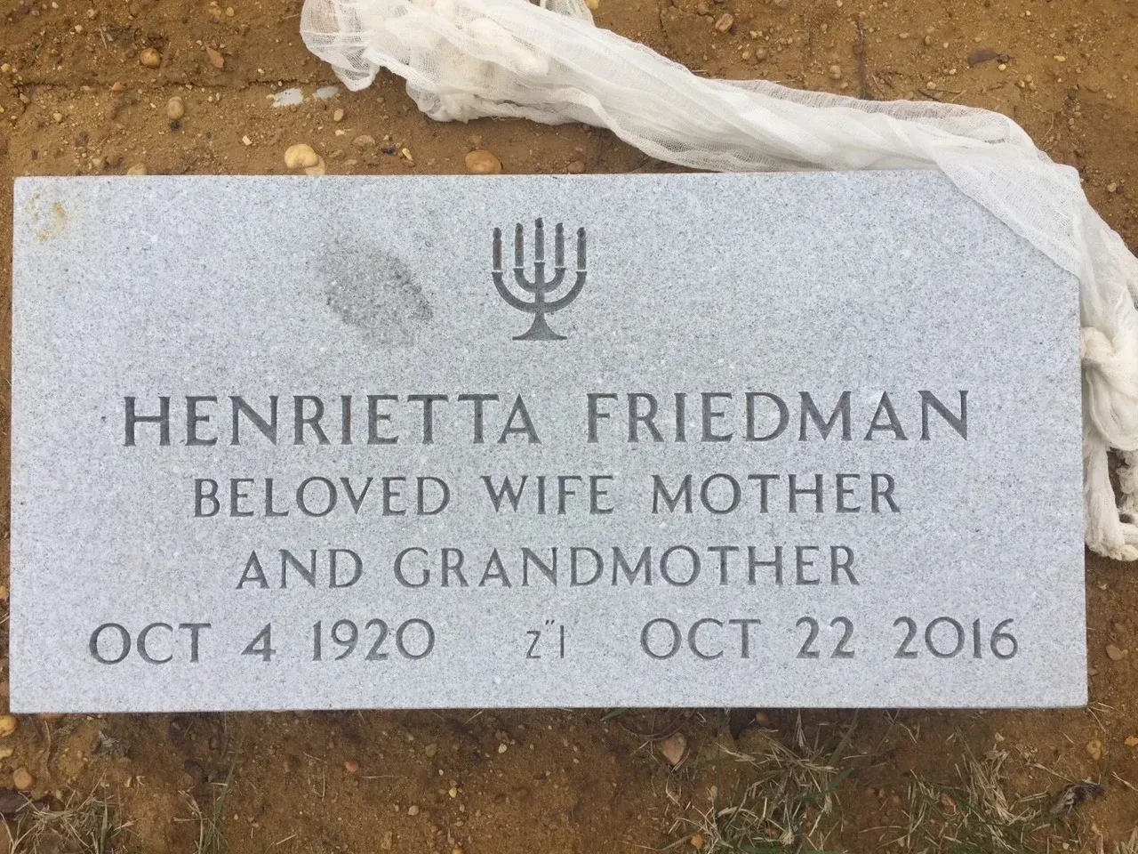 Gravestone for Henrietta Friedman, with memorial text and dates, set in dirt and stone