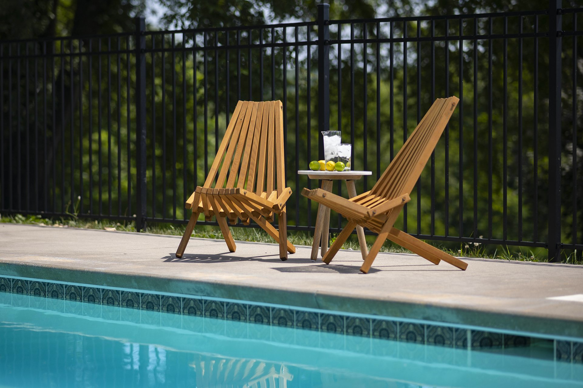 Two wooden chairs and a table are sitting next to a swimming pool.