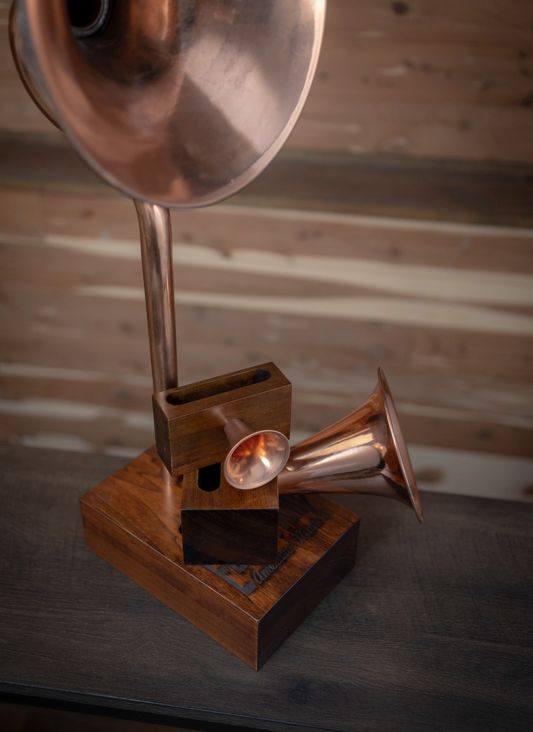 A copper phonograph is sitting on a wooden table.