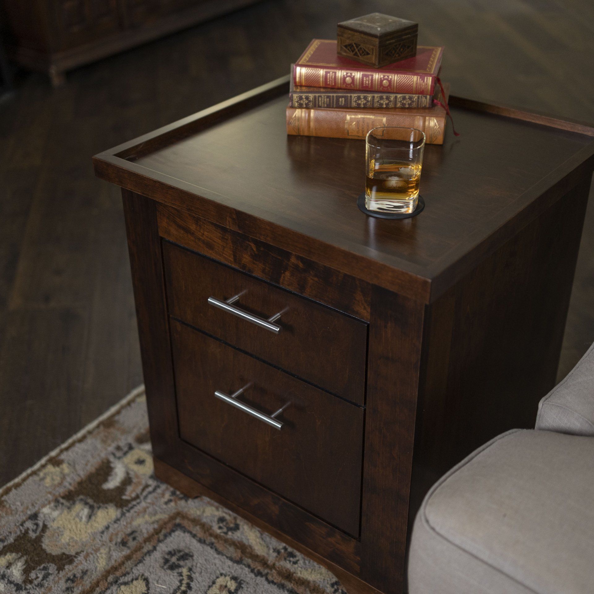 A nightstand with books and a glass of whiskey on it