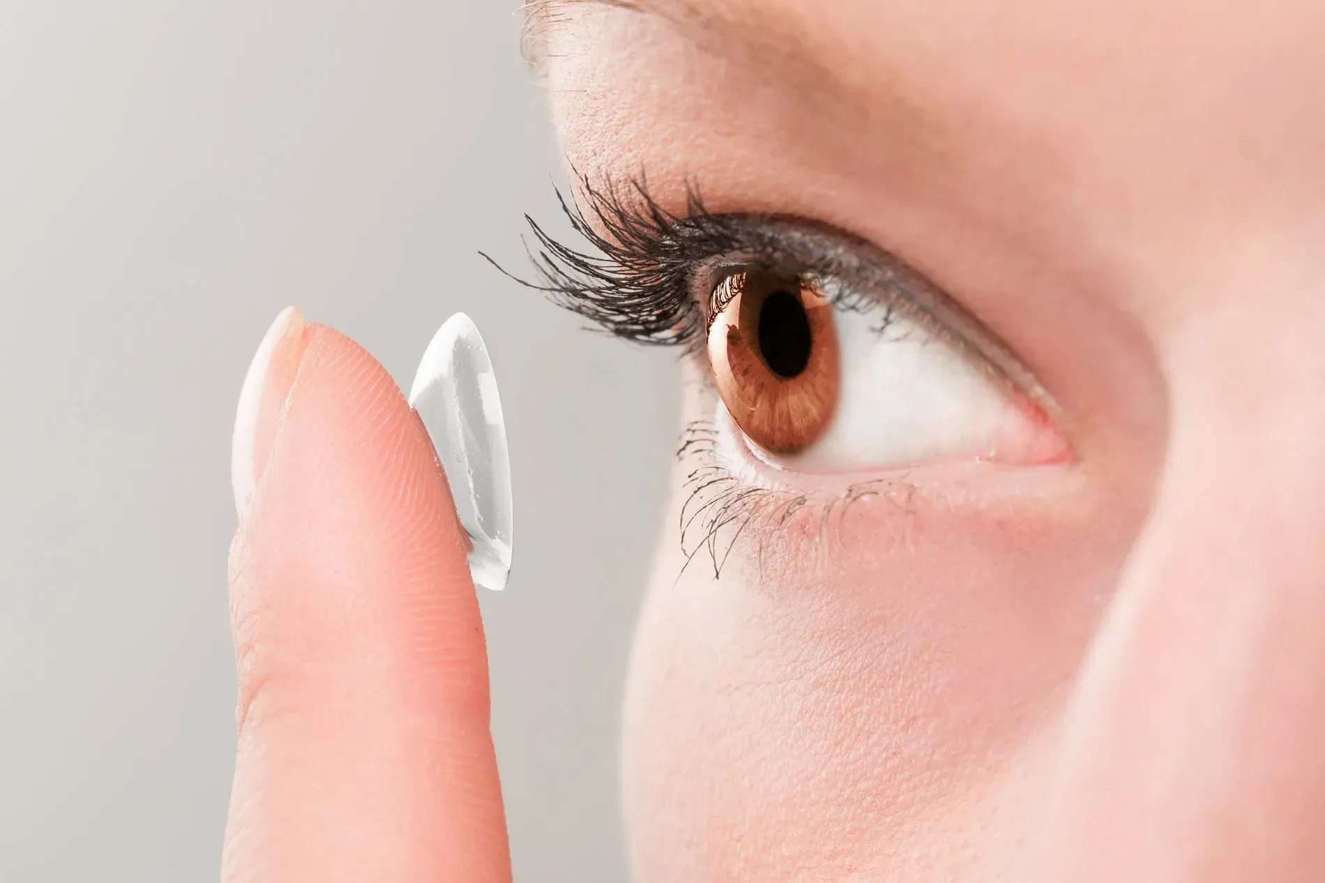 Person placing a contact lens on their brown eye.