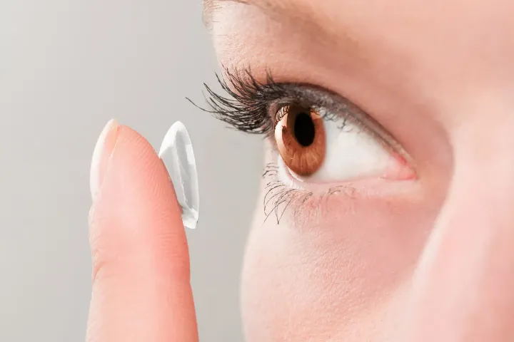 Person placing a contact lens on their brown eye.