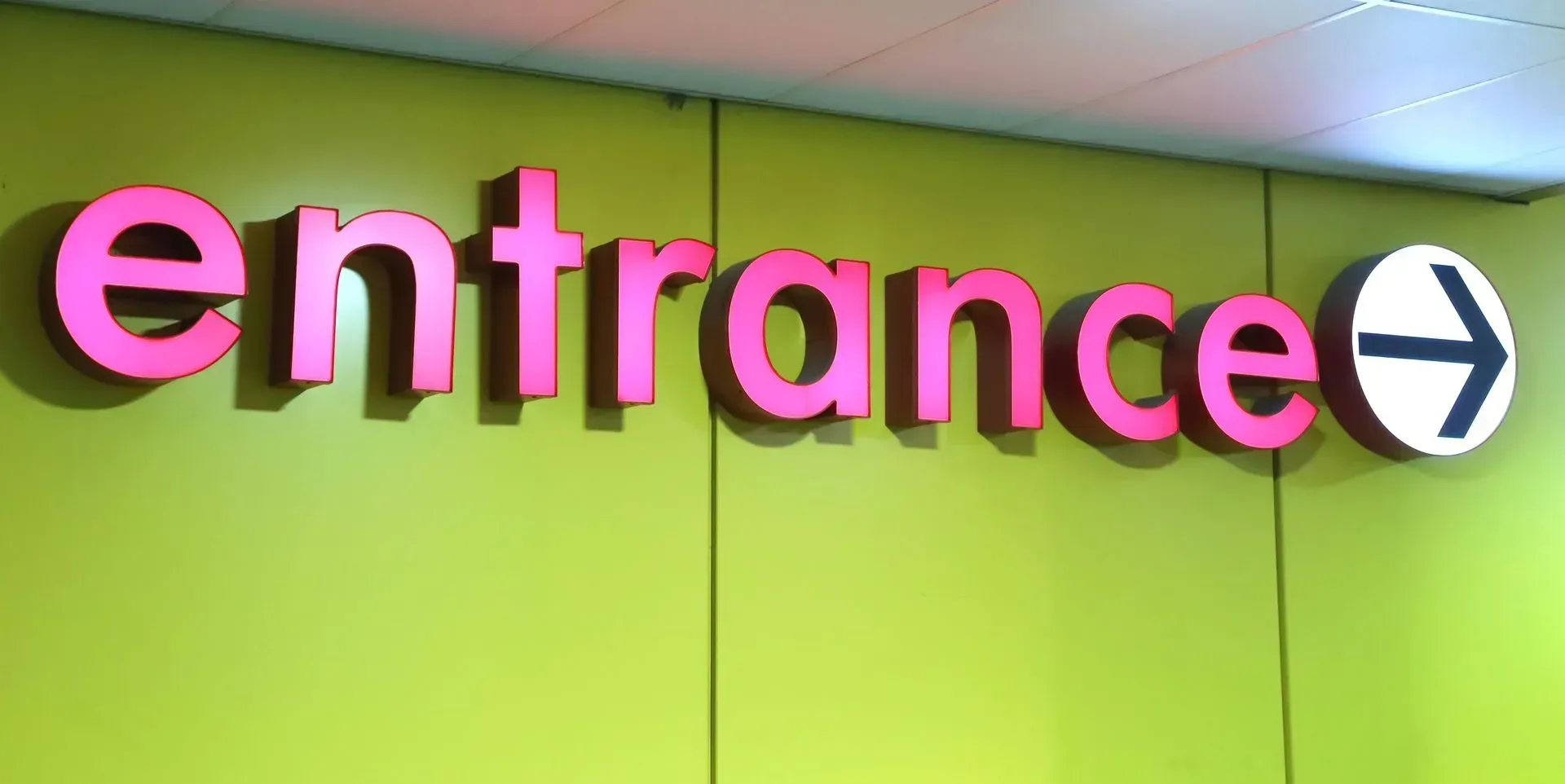 Pink “entrance” sign on a green wall with a white arrow pointing right