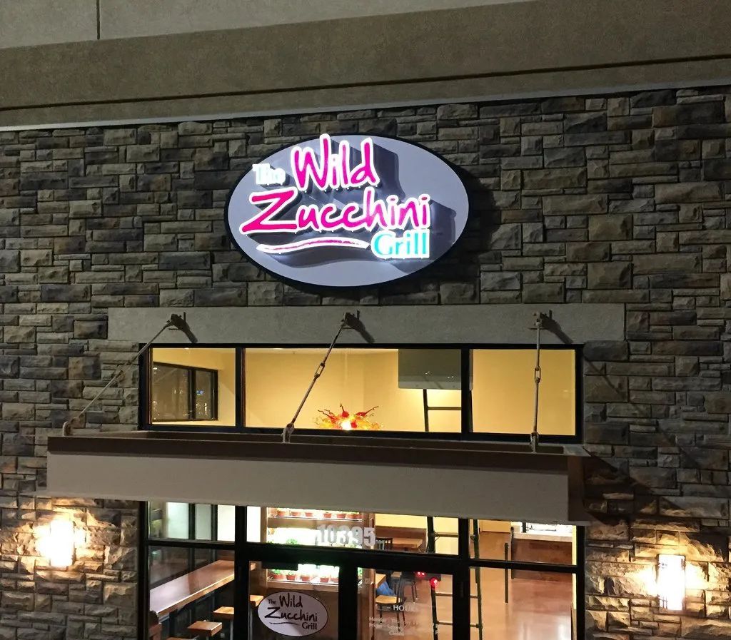 Wild Zucchini Grill sign on a stone building at night, with warm lights glowing inside.