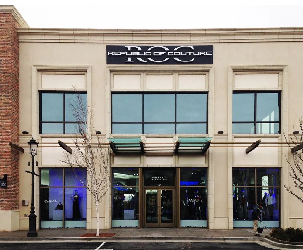 Street view of a two-story storefront with large windows and a blue sign above the entrance