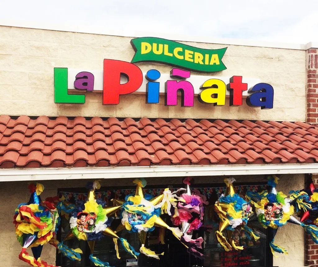 Colorful Dulceria La Piñata storefront sign above a tiled roof with hanging piñatas underneath