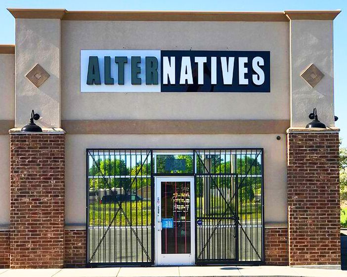 Storefront with “ALTERNATIVES” sign above a gated entrance and glass door