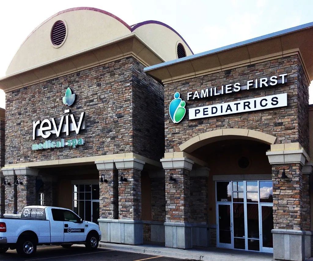 Reviv and Families First Pediatrics storefront in a stone shopping center with a parked white pickup truck