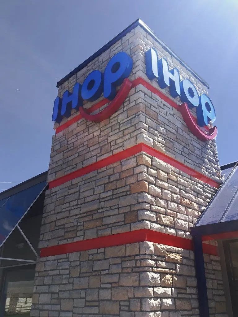 IHOP restaurant sign on a stone tower with red trim against a blue sky