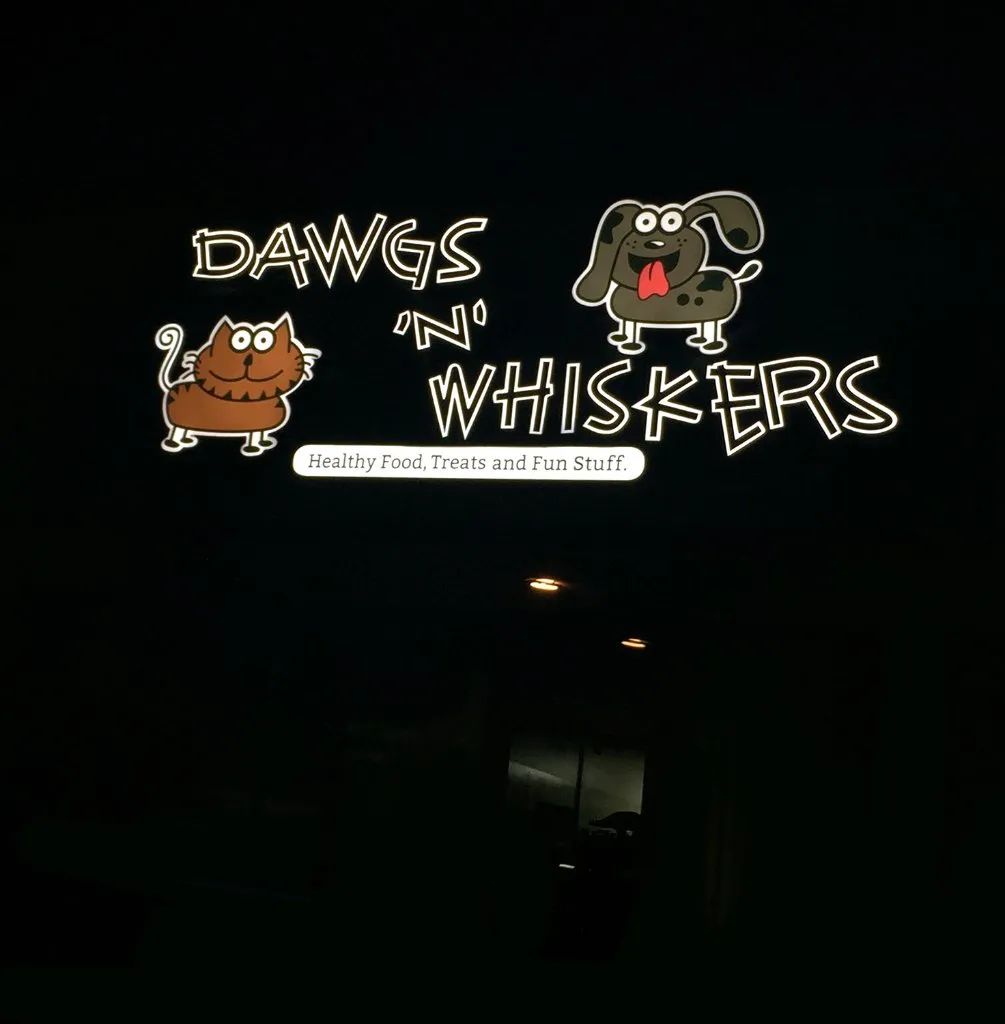 Neon sign for “Dawgs ’n’ Whiskers” with cartoon dog and cat on a dark background.