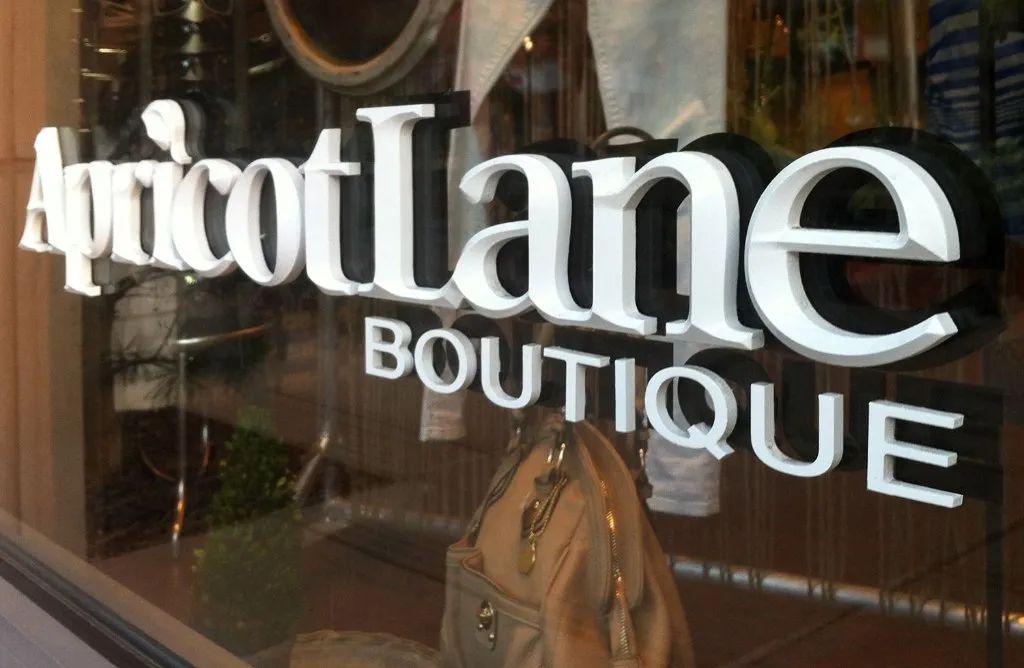 Boutique storefront window with large white “Apricot Lane” lettering and a handbag display inside