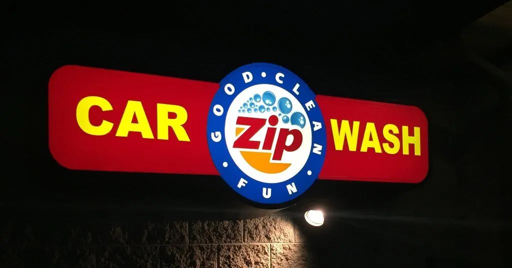 Goodz Car Wash illuminated sign at night with red background, yellow text, and blue center logo
