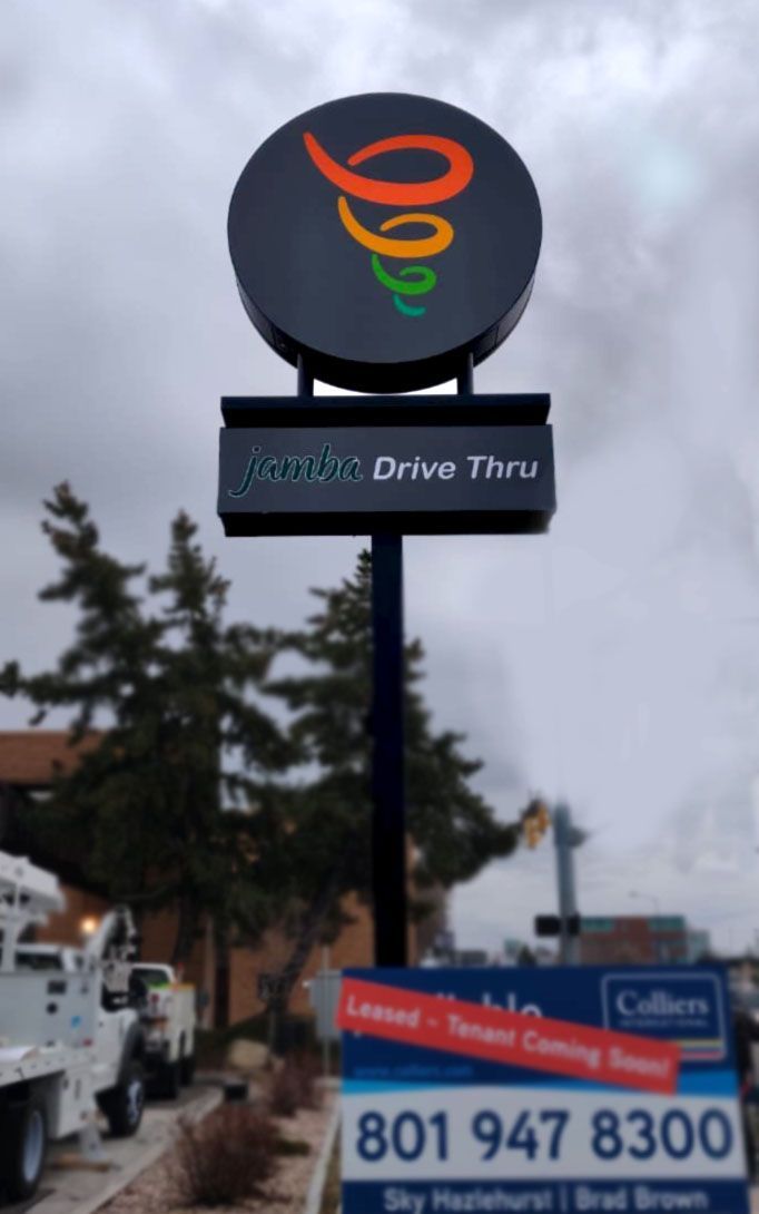 Spark Drive Thru sign with colorful swirl logo on a roadside pole above a phone-number banner.