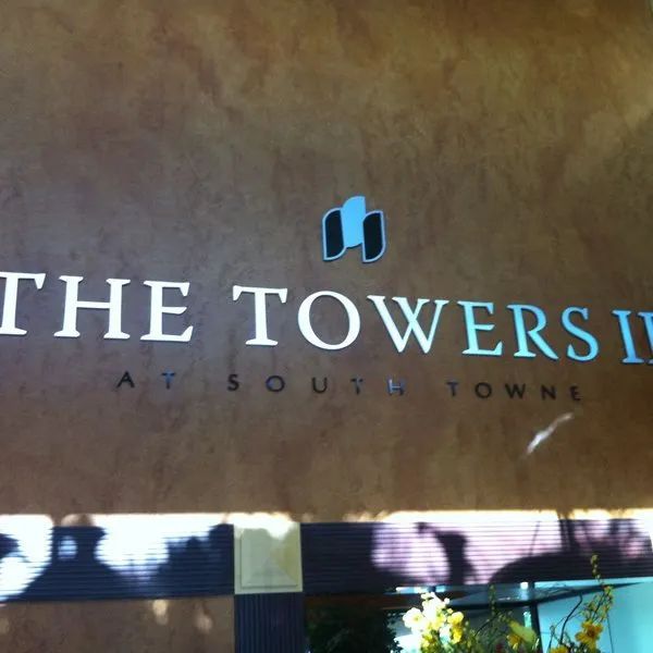 Sign for The Towers at South Town on a brown wall with a blue logo