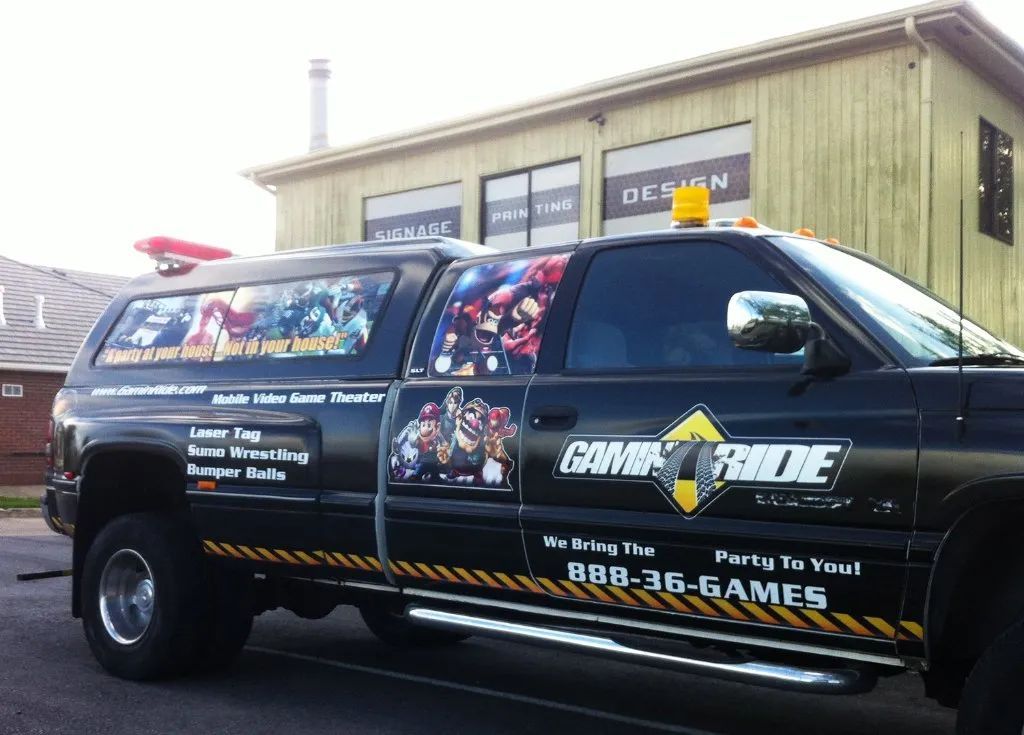 Black GameRide-branded van parked outside a building, with colorful gaming graphics on the side