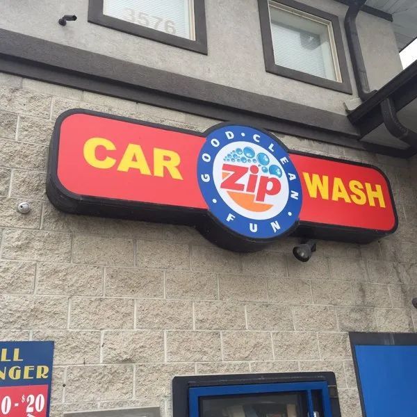 Red and blue “CAR WASH” sign on a building exterior with a round “Zip” logo.