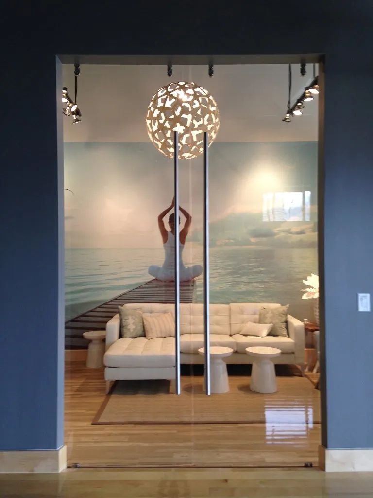 Modern lounge with white sofa behind glass doors, ocean mural, and hanging spherical light.