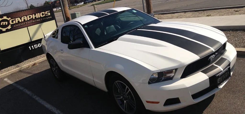 White sports car with black racing stripes parked outdoors beside a sign