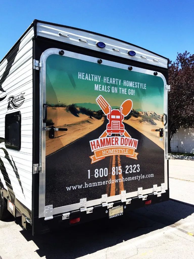 Hammer Down trailer parked outdoors, with a large sports-themed ad and phone number on the back.
