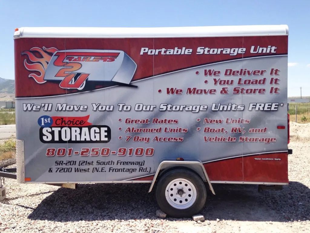 Red and silver portable storage trailer with company branding and a large wheel on a road
