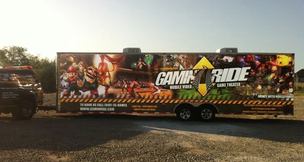 Large black trailer with colorful action-game graphics parked on gravel outdoors at sunset