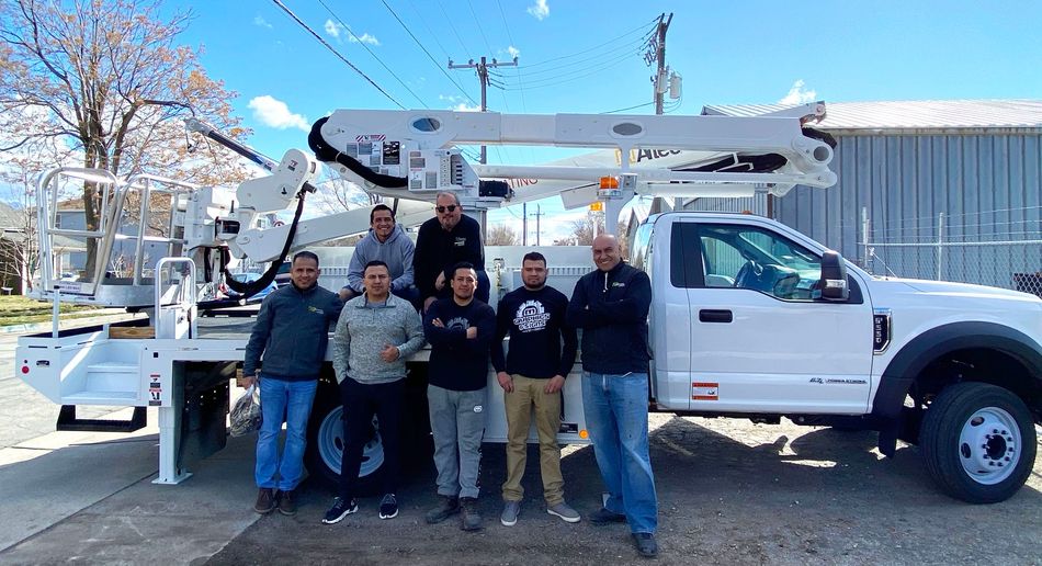 Group of people posing beside a white utility truck with an extended work boom outdoors
