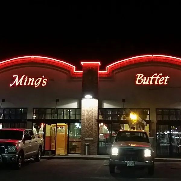 Ming's Buffet storefront at night with red neon signage and parked vehicles