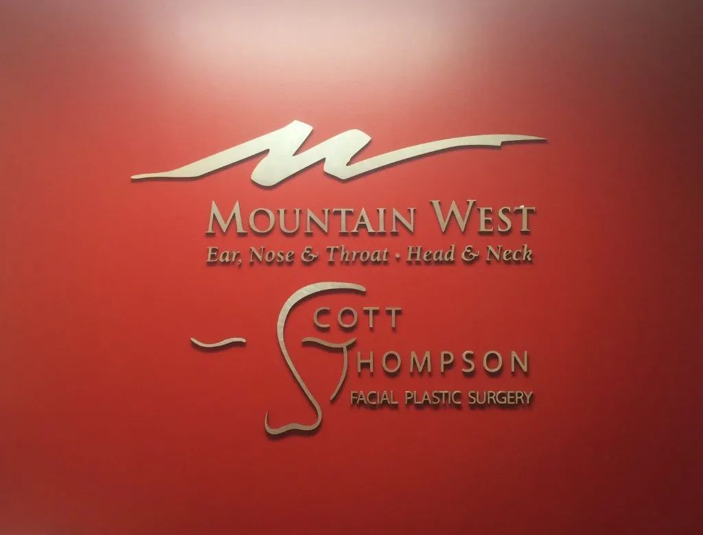Red background with Mountain West and Scott Thompson facial plastic surgery logo in gold and white