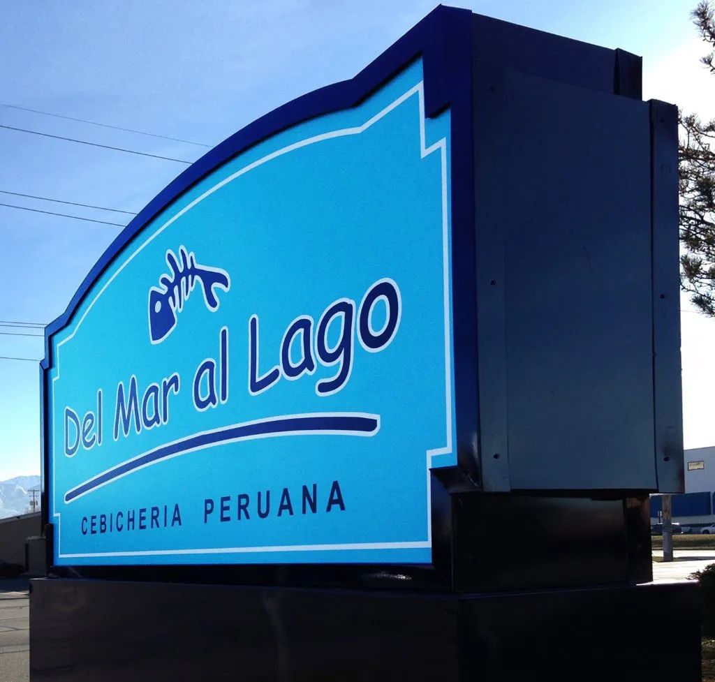 Blue restaurant sign reading “Del Mar al Lago” with “Cocineria Peruana” underneath.