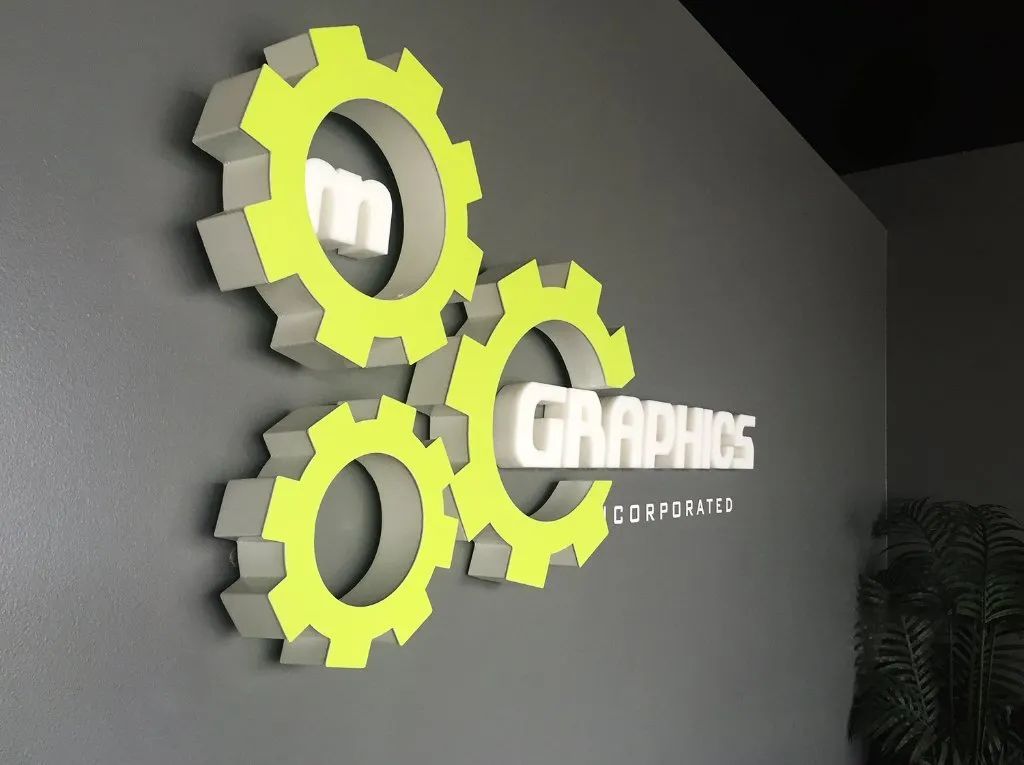 Gray wall logo with neon yellow gears and the word “Graphics” in white.