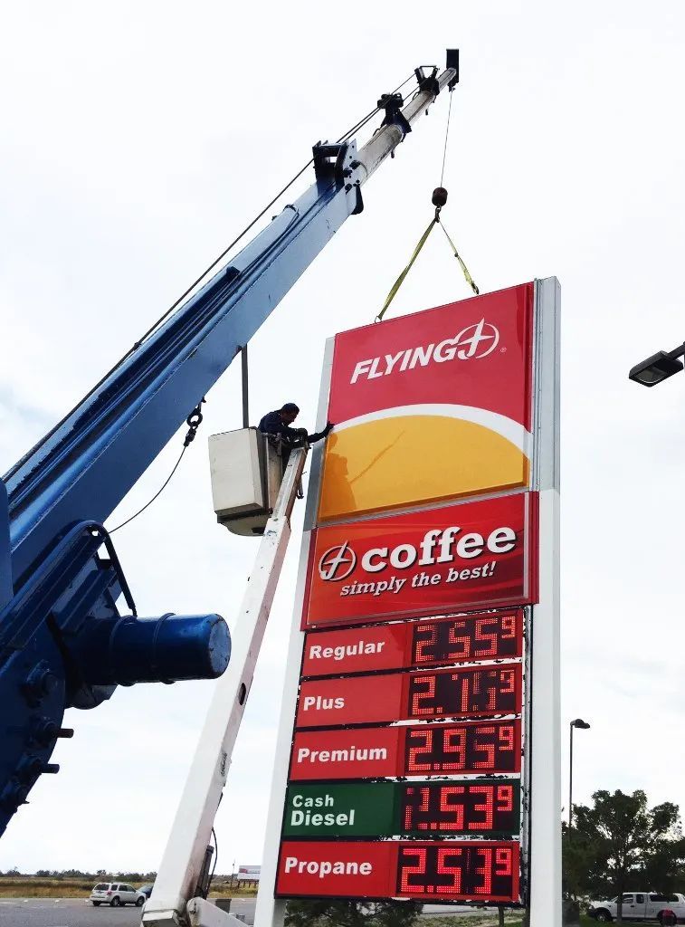 Crane lifts a red Flybe coffee sign at a roadside gas station price board