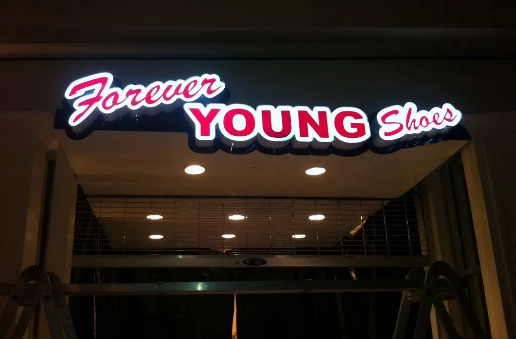 Neon sign reading “Forever Young Shoes” above a storefront entrance at night