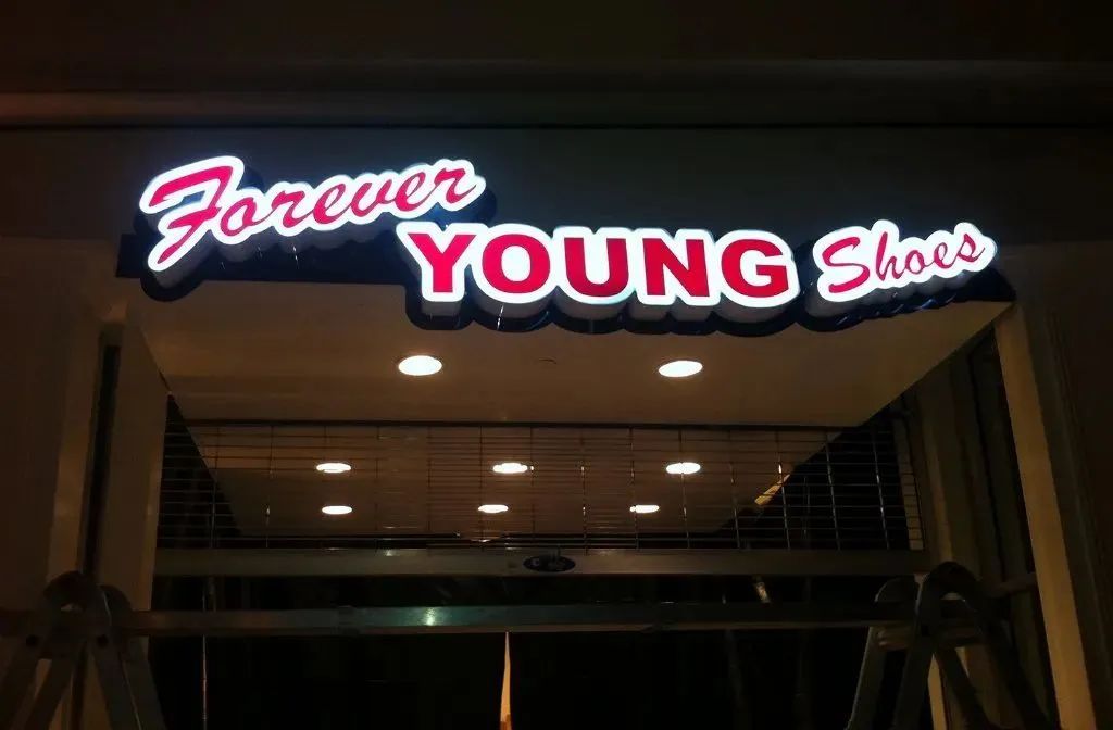 Storefront sign reading “Forever Young Shoes” glowing in red and white above an entrance