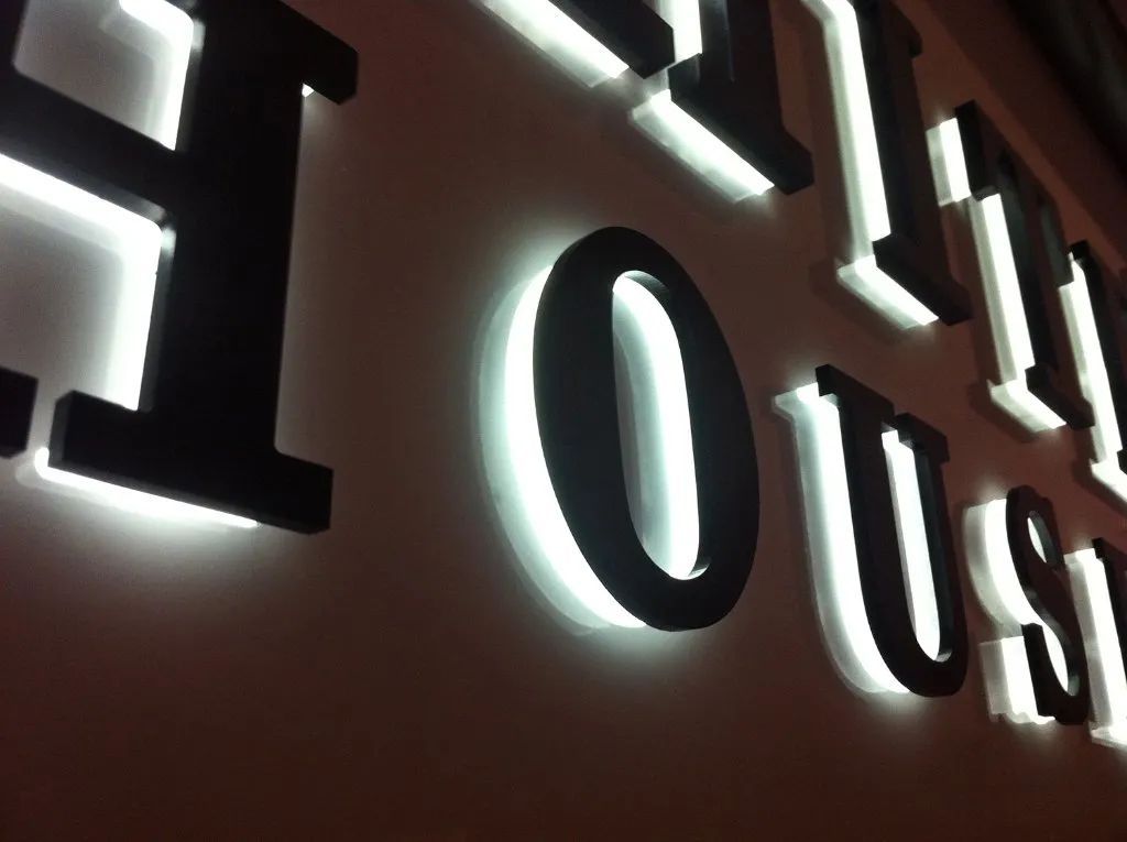 Backlit house sign reading “HOUSE” in white letters on a dark wall