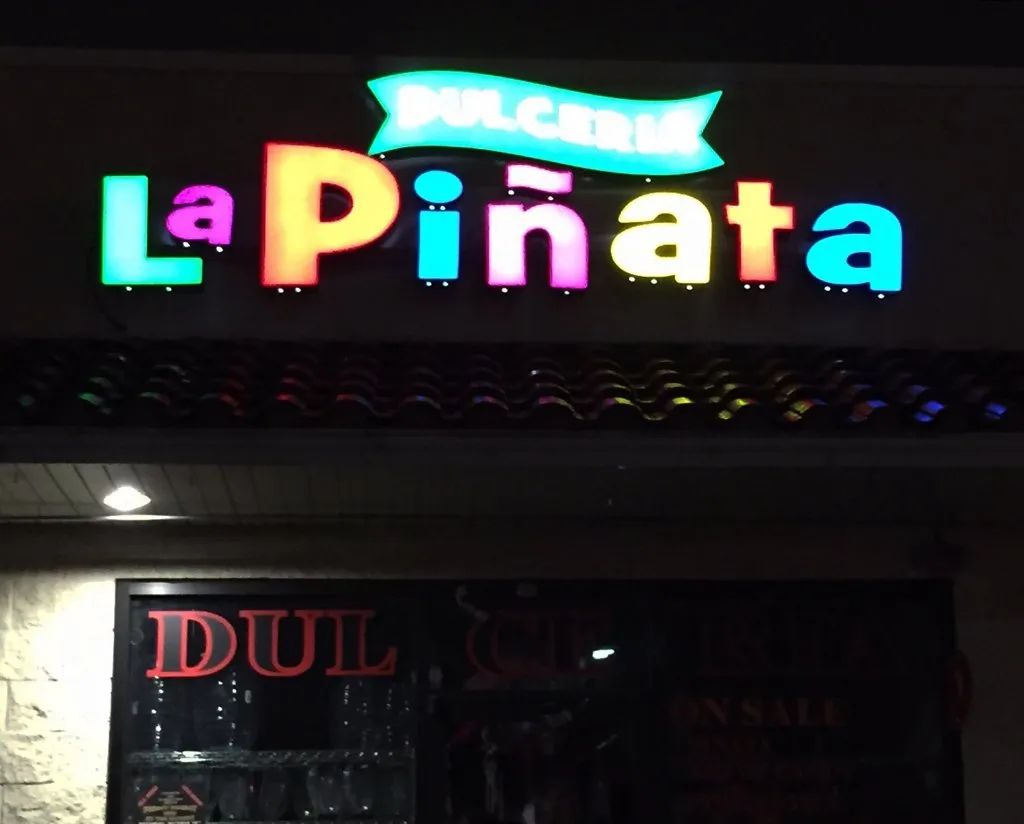 Neon sign reading “La Piñata” in colorful letters above a storefront at night