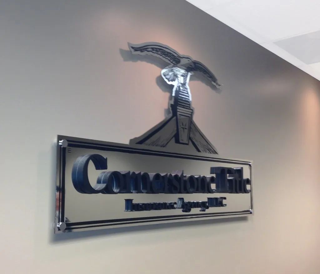 Chrome wall sign for “Cornerstone Title” with a house roof logo on a gray office wall