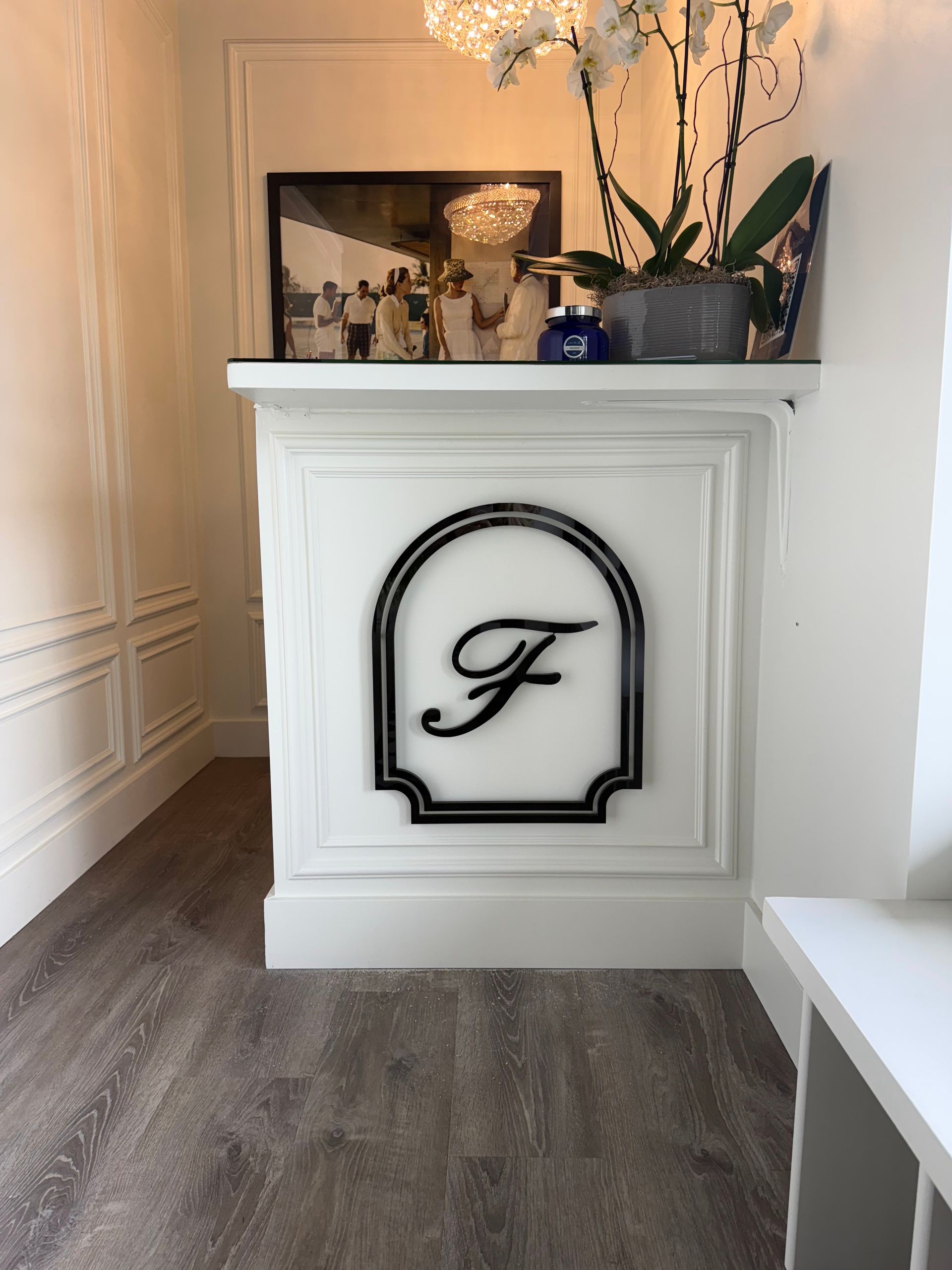White decorative fireplace mantel with black monogram, plants, flowers, and framed art in a bright room