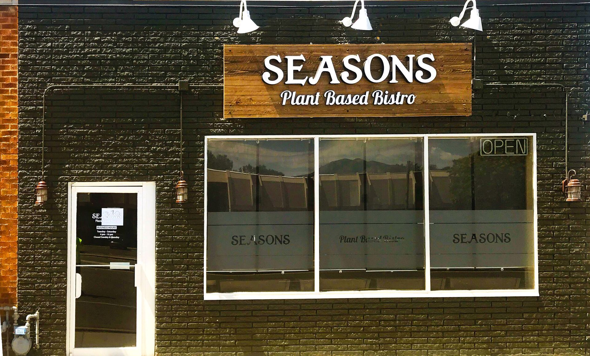 Storefront with a wooden sign reading “SEASONS,” dark exterior, and large front windows.