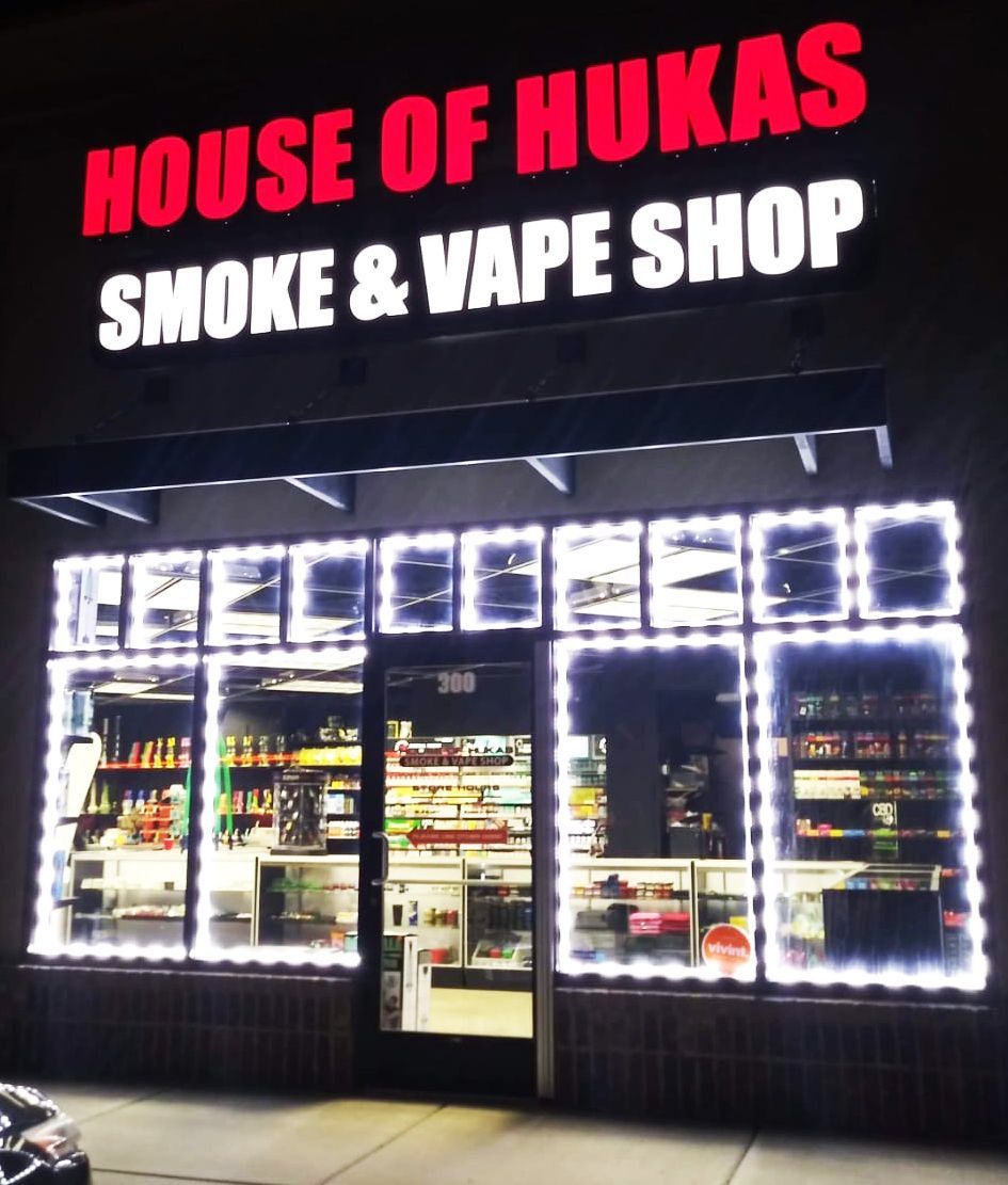 Nighttime exterior of House of Hukas smoke and vape shop, lit by bright white window lights.