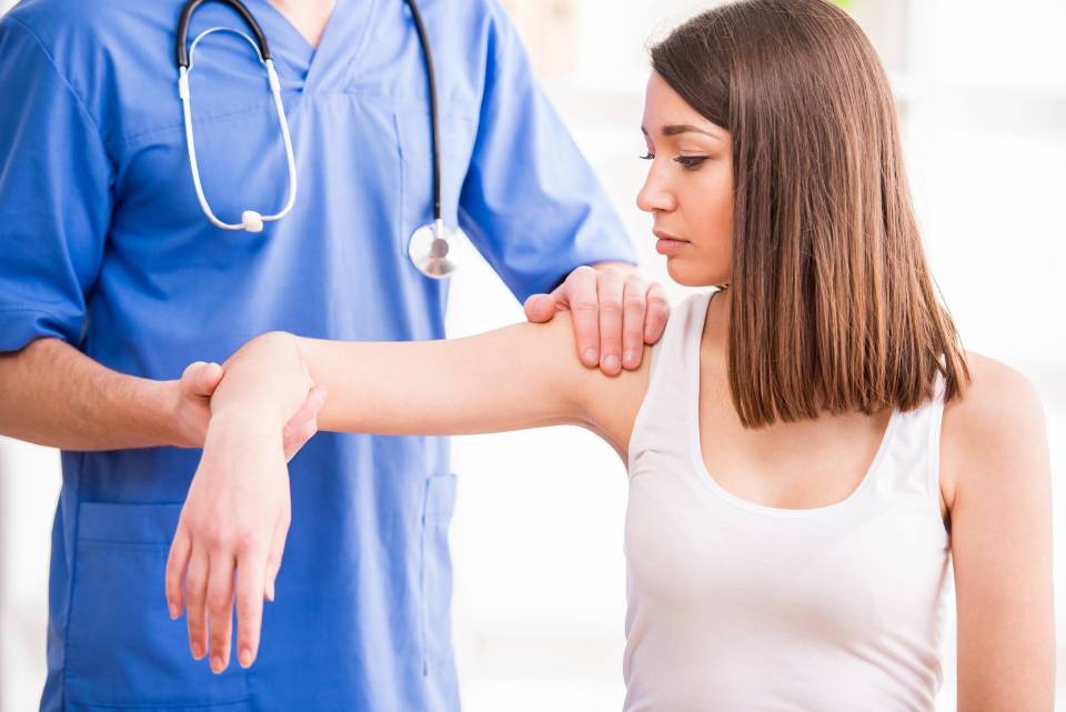 Medico che esamina il braccio di un paziente; l'ambiente sembra essere quello di uno studio medico.